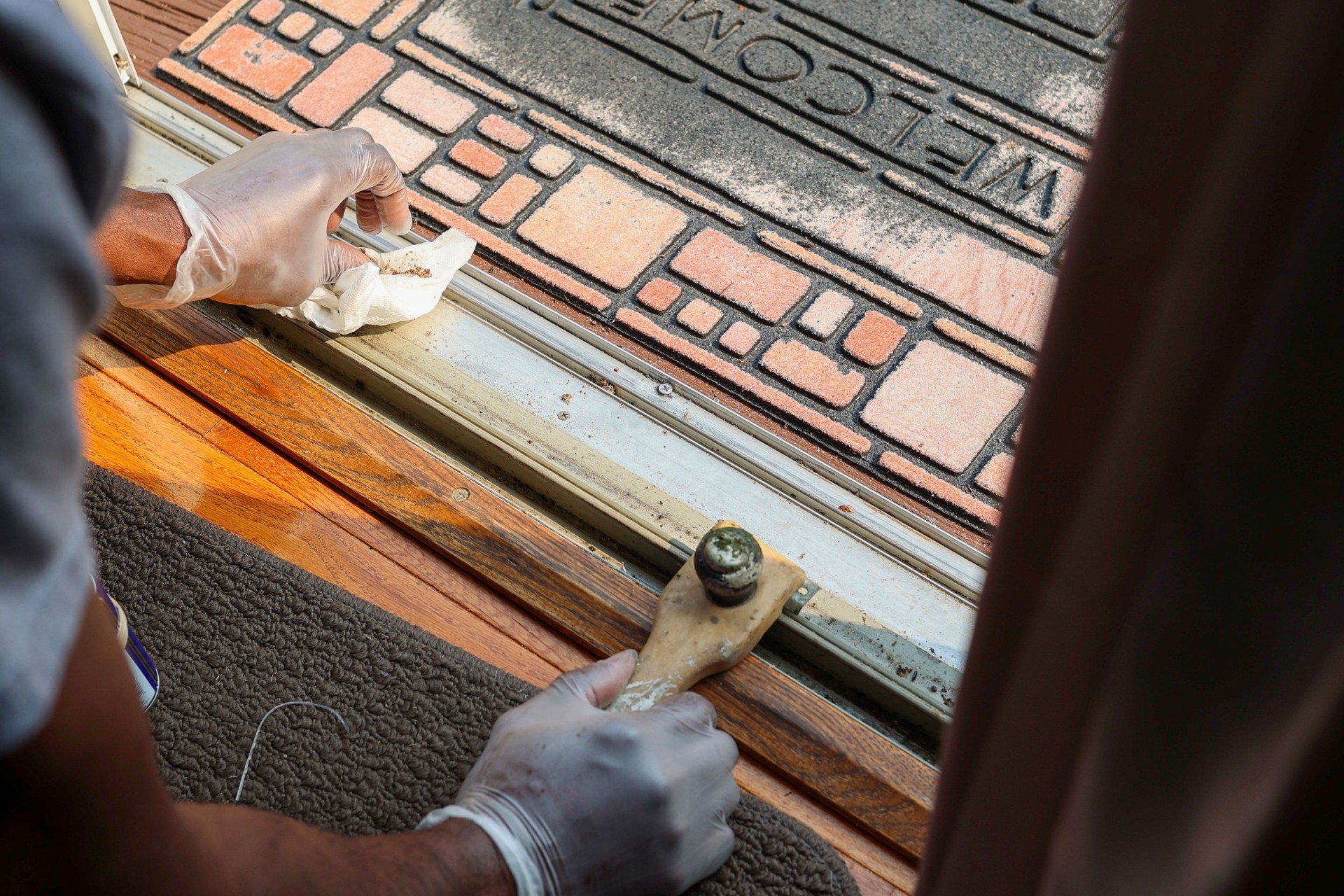 A black man cleaning dirty tracks on a patio sliding door